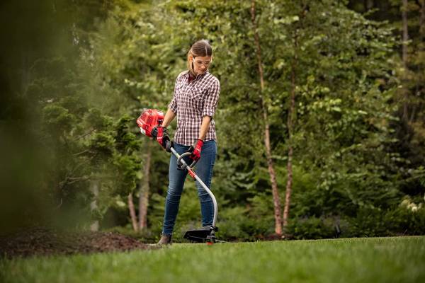 A woman edging the lawn with a curved shaft trimmer—how to edge with a curved shaft trimmer