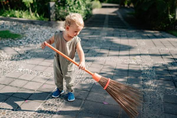 Charming Child Sweeping Concrete Pavement with Broomstick—looking after a large garden